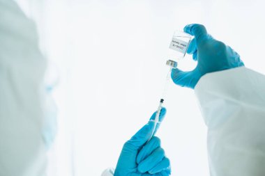 Koronavirüs için kullanılan iğne, kişisel koruma ekipmanı ya da PPE giysisini gösteren bir tıbbi PPE giysisi içinde tanınmayan bir uzman doktor..