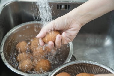 Tanınmayan Asyalı ev hanımı lavaboda çiğ yumurta yıkıyor yakından, kadın mutfakta pişirmeden önce kirli yumurta kabuğunu temizliyor ve hazırlıyor..