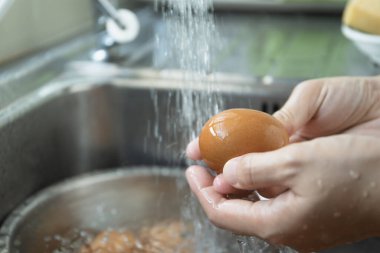 Tanınmayan Asyalı ev hanımı lavaboda çiğ yumurta yıkıyor yakından, kadın mutfakta pişirmeden önce kirli yumurta kabuğunu temizliyor ve hazırlıyor..