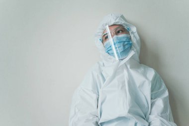 Stresli, endişeli Asyalı ilaç personeli duvardaki sandalyede oturuyor, sağlık çalışanı hastanede çok çalışıyor. Aşırı çalışan sağlık görevlisi - hemşire yorgun hissediyor.