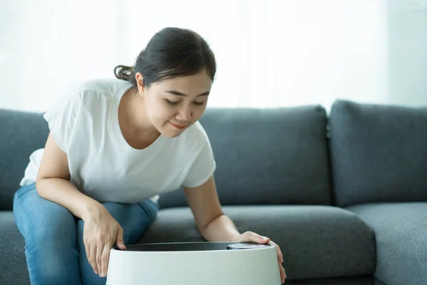 Asian woman turning on and using the modern air purifier while staying in the living room, air purifier is a popular appliance - household electricity. Air purifier can help to purify the air.