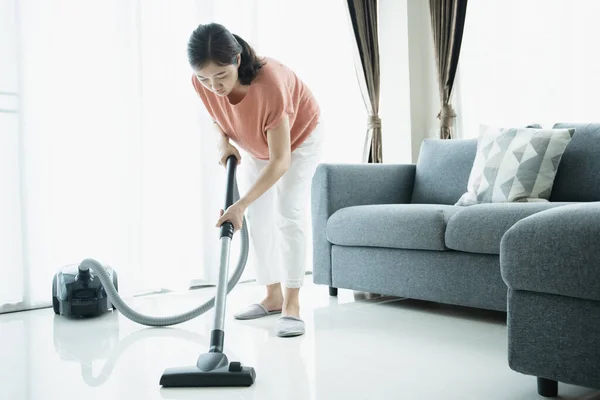 Asian young housekeeper using vacuum machine to clean a dirty floor in the living room close up with copyspace. Housewife vacuuming a floor and sofa in living room.