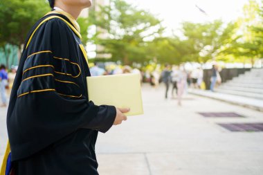 Üniversite mezuniyet töreninde diplomaları elinde tutan mutlu Asyalı öğrenci. Önlük giymiş yüksek lisans öğrencisi elinde fotoğrafçılık diploması tutuyor..