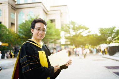 Üniversite mezuniyet töreninde diplomaları elinde tutan mutlu Asyalı öğrenci. Önlük giymiş yüksek lisans öğrencisi elinde fotoğrafçılık diploması tutuyor..