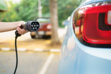 EV şarj istasyonunda AC tip 2 EV şarj konnektörü tutan tanınmayan Asyalı kadın, bir EV-elektrikli araç konnektörü hazırlayan kadın bir aracı şarj etmek için.
