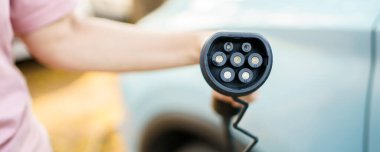 EV şarj istasyonunda AC tip 2 EV şarj konnektörü tutan tanınmayan Asyalı kadın, bir EV-elektrikli araç konnektörü hazırlayan kadın bir aracı şarj etmek için.