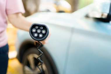 EV şarj istasyonunda AC tip 2 EV şarj konnektörü tutan tanınmayan Asyalı kadın, bir EV-elektrikli araç konnektörü hazırlayan kadın bir aracı şarj etmek için.