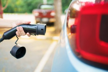 EV şarj istasyonunda AC tip 2 EV şarj konnektörü tutan tanınmayan Asyalı kadın, bir EV-elektrikli araç konnektörü hazırlayan kadın bir aracı şarj etmek için.