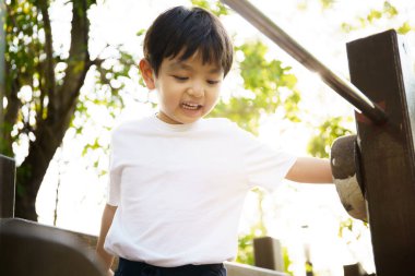Mutlu Asyalı çocuk, babasıyla parkta oynamaktan ve yürümekten zevk alıyor. Asyalı çocuk, babasına bakarken çok güzel gülümsüyor. Parktaki ve parktaki küçük çocuk portresi.