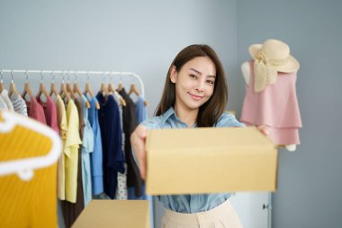 Kameraya karton bir paket kutusu gösteren mutlu bir Asyalı genç kadın, çevrimiçi satış ya da ekommerce konsepti. Kadın çevrimiçi satıcı çevrimiçi pazar platformu üzerinden kıyafet satıyor.