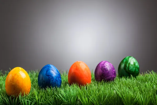 Gefärbte Ostereier im Gras, grauer Hintergrund — Stockfoto