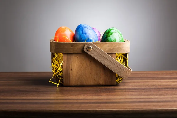 Cesta, ovos de páscoa coloridos na mesa, fundo cinza — Fotografia de Stock