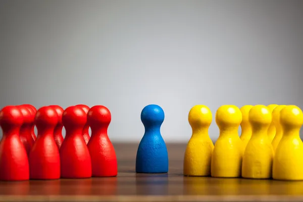Single blue pawn figure between red and yellow groups — Stock Photo, Image
