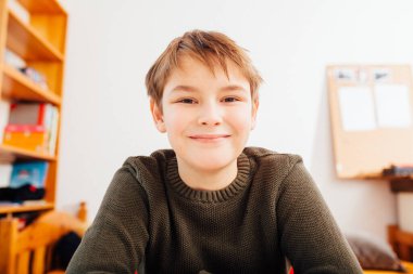 Ten year old school boy smiling happy in home video schooling situation, close up looking into wide angle camera