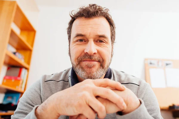 Mature adult male teacher in home schooling video chat conference, similing friendly into camera, close up portrait with wide angle