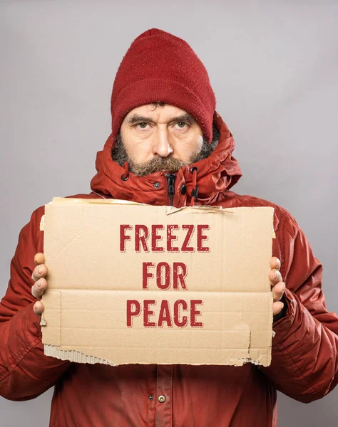 Mature man with cardboard sign with Freeze for Peace motivational message text  in thick winter coat at freezing cold temperatures