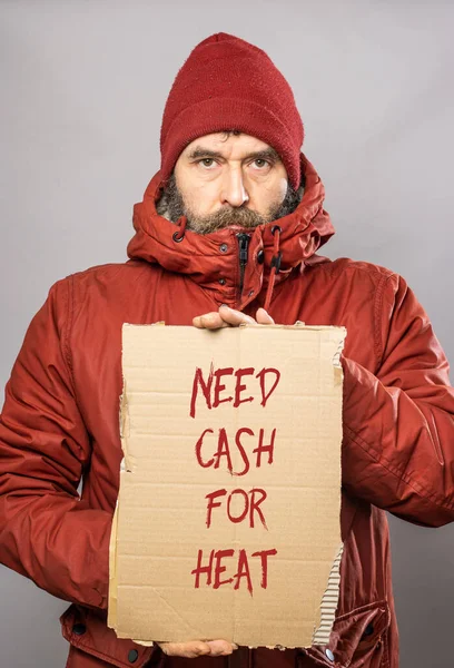 Mature man with cardboard sign with Need Cash for Heat text  in thick winter coat at freezing cold temperatures