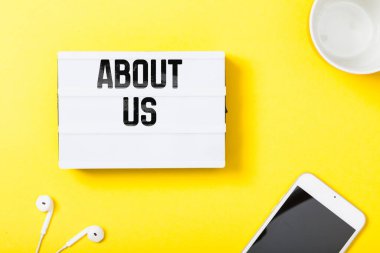 About Us headline in notebook with phone, headphones and coffee mug on yellow background
