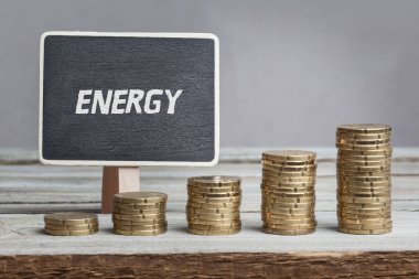 Sözcük Enerjisi kara tahtada ve yükselen madeni para desteleri tahta masada yazılı.