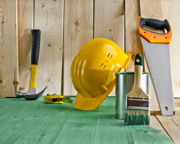 Grüner Holzboden mit Pinsel, Farbe, Säge und gelbem Helm — Stockfoto