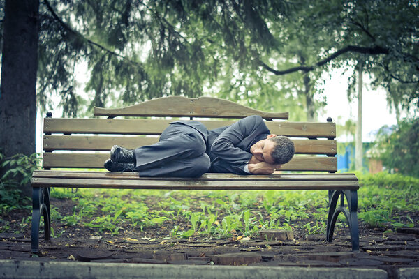 man in a suit sleeping on the street bench