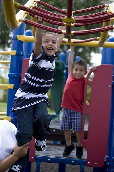 Hispanic brothers swinging from monkey bars — Stock Photo, Image