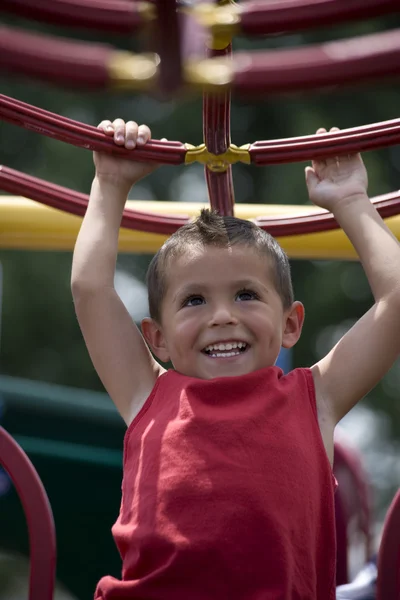 HIspanic little boy swinging from monkey bars — Stock Photo, Image