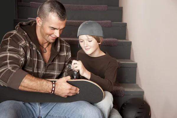 Jonge volwassen man helpen een adolescent jongen met zijn skateboard — Stockfoto