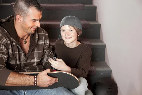 Young adult man helping an adolescent boy with his skateboard — Stock Photo, Image