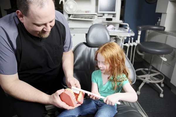 Dentiste montrant à une petite fille comment se brosser les dents — Photo