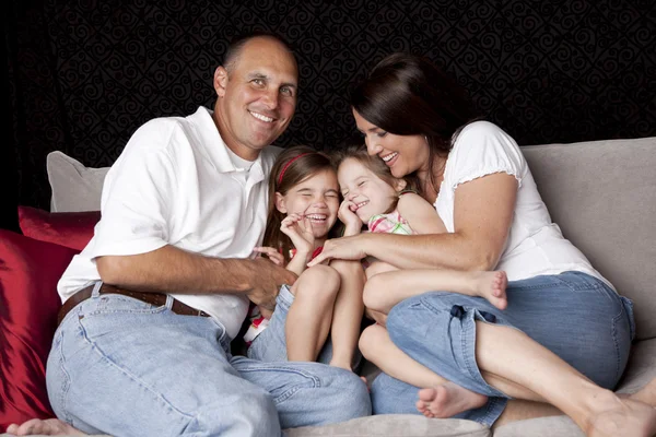 Família sorridente com dois filhotes brincando no sofá — Fotografia de Stock