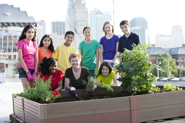 Niños de diferentes etnias que cultivan un huerto con una mujer adulta —  Fotos de Stock