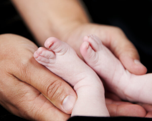 Father's hands holding tiny feet of newborn baby