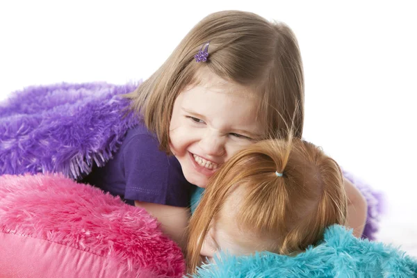 Dos hermanas jugando, abrazándose y luchando entre almohadas coloridas — Foto de Stock