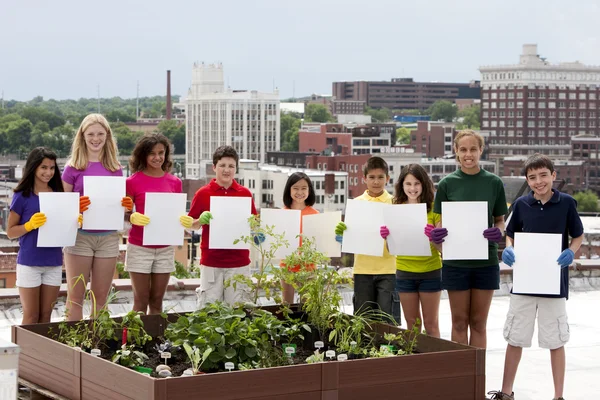 Diversos niños por jardín urbano en la azotea sosteniendo carteles en blanco Fotos de stock libres de derechos