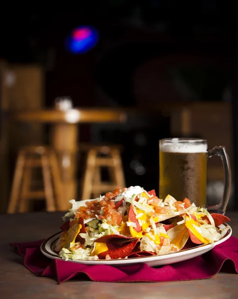 Essen und Trinken. eine Vorspeise aus würzigen Nachos mit einem frostigen Becher Bier — Stockfoto