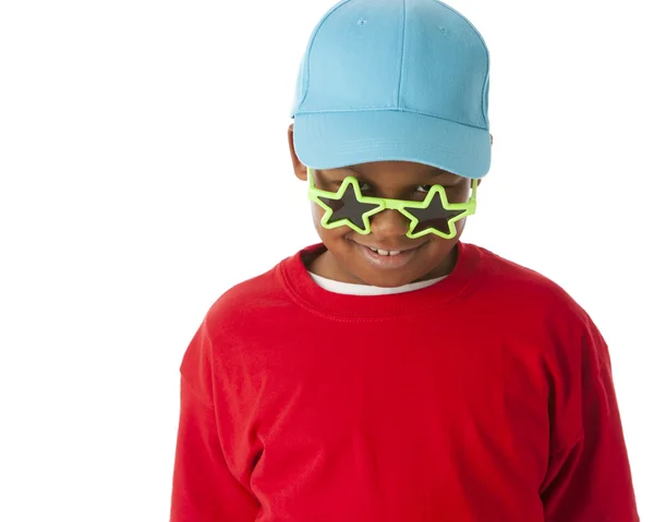 Echt. schwarzer kleiner Junge trägt ein knallrotes Hemd mit Baseballmütze und lugt über eine alberne Sonnenbrille — Stockfoto