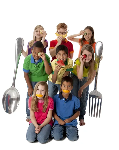 Alimentación Saludable. Diverso grupo de niños sosteniendo juguetonamente una variedad de frutas y verduras saludables con un tenedor gigante y una cuchara —  Fotos de Stock
