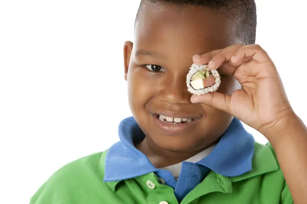 Healthy Eating. frican american little boy holding a piece of sushi up to his eye — Stock Photo, Image