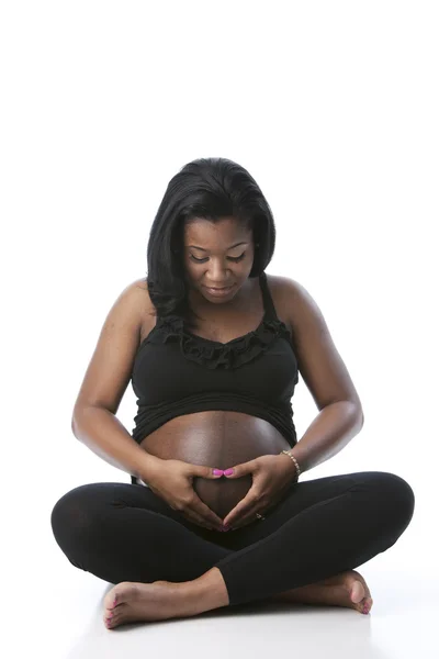 De verdad. Negro embarazada madre mirando tiernamente hacia abajo en su abdomen y haciendo un corazón con sus manos —  Fotos de Stock