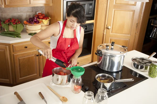 Konserven. Junge erwachsene Frau mit gemischter Rasse, die Obst und Gemüse aus eigenem Anbau einschenkt — Stockfoto