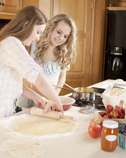 Cozinhar. Namoradas adolescentes caucasianas rolando massa para fazer uma torta de frutas com frutas caseiras na cozinha — Fotografia de Stock