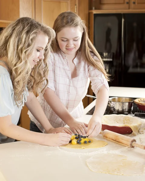 Bakken. Kaukasische tiener vriendinnen maken van een taart fruit en gebak met homegrown vruchten in de keuken — Stockfoto