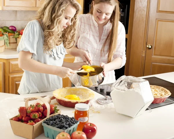 Baking: Caucasian caucasian teenage girlfriends making a fruit pie with homegrown fruits in the kitchen — Stock Photo, Image