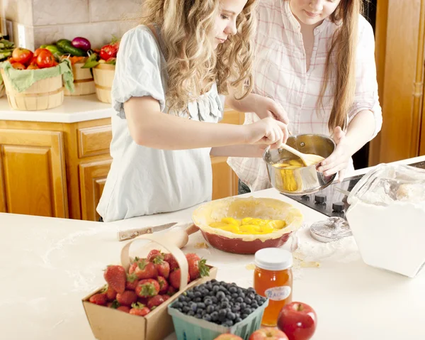 Baking: Caucasian caucasian teenage girlfriends making a fruit pie with homegrown fruits in the kitchen — Stock Photo, Image