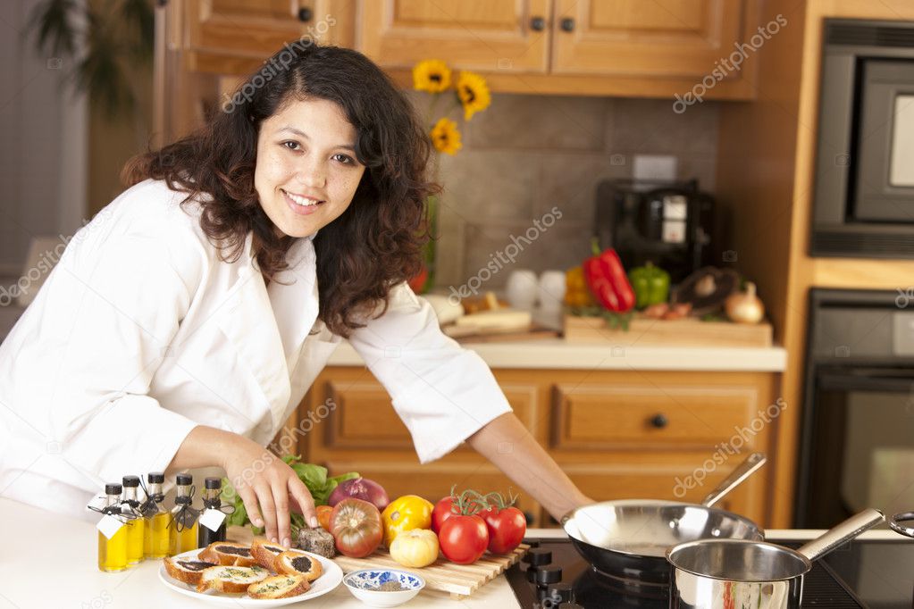 Real. Mixed race young adult woman cooking bruschetta and a healthy meal in her kitchen