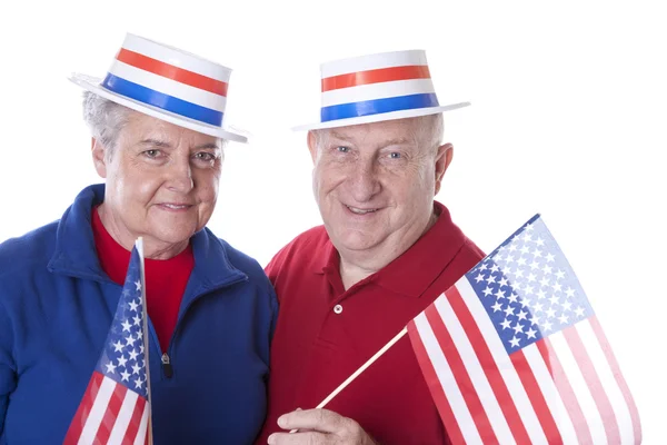Casal patriótico adulto caucasiano acenando com bandeiras americanas e usando chapéus com estrelas e listras — Fotografia de Stock