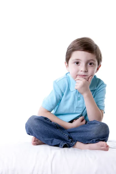 Niño caucásico sentado con las piernas cruzadas con la mano en la barbilla como si estuviera pensando — Foto de Stock