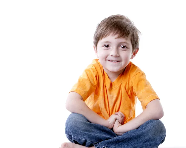 Улыбающийся белый мальчик, сидящий со скрещенными ногами — стоковое фото