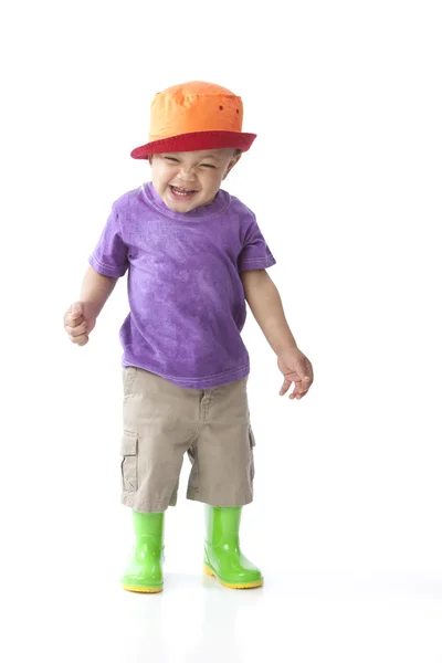 Criança negra afro-americana menino pequeno vestindo botas coloridas de chuva com uma camisa roxa e chapéu laranja — Fotografia de Stock